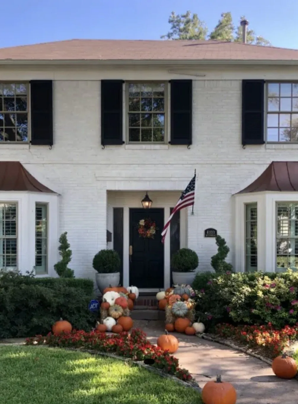 Standard front porch layered with roughly 25 to 35 real uncarved pumpkins across the upper steps